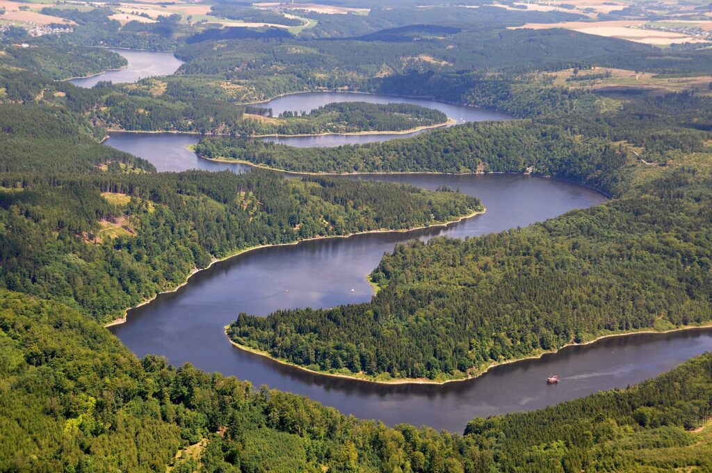 Eine Luftaufnahme von der Bleilochtalsperre, die eine Flusslandschaft umgeben von grünen Wäldern zeigt.
