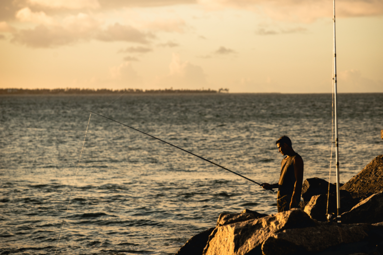 Ein Angler, der an einem Sonnenuntergang am Meeresufer angelt.