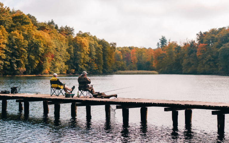 2 Angler, die auf einem Holzsteg sitzen und fischen.