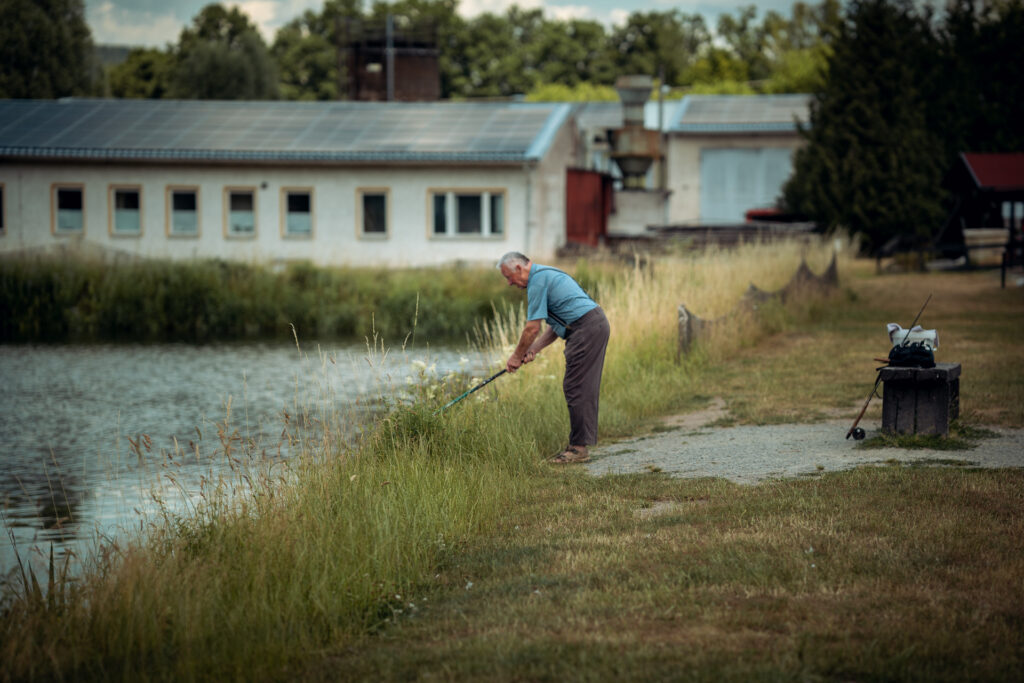 Ein alter Mann, der am Ufer eine Angelrute hält und fischt.