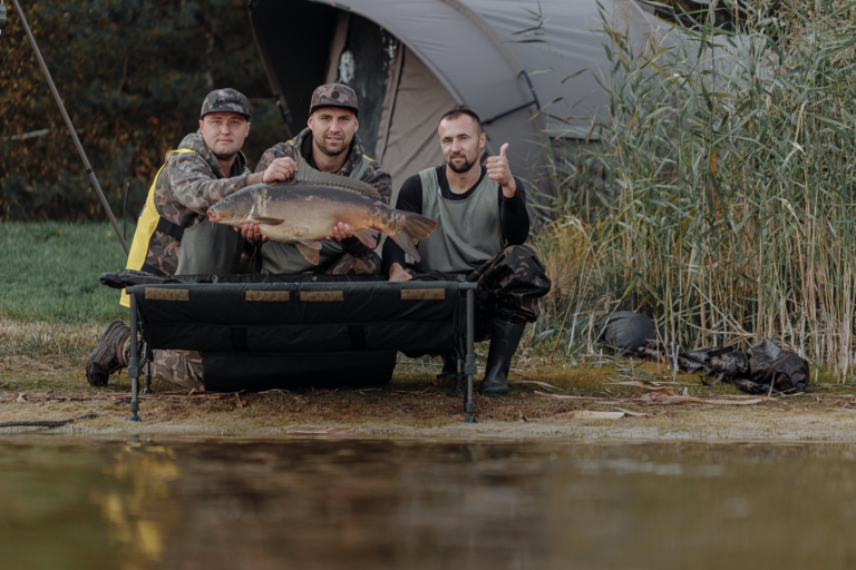 3 Angler, die einem großen Fisch halten, wobei im Hintergrund ein Zelt steht.