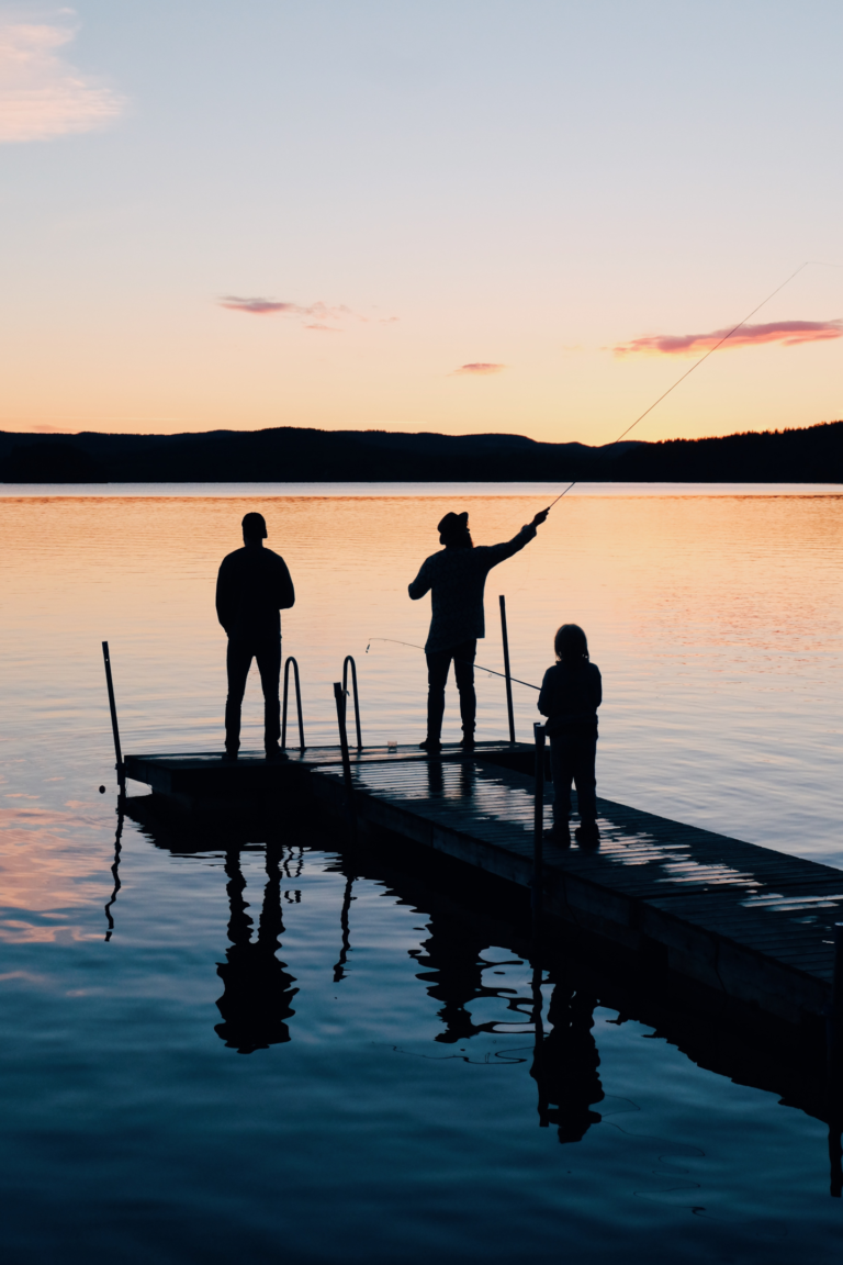 Drei Personen beim Angeln auf einem hölzernen Fischerdock, mit Blick auf das Wasser.