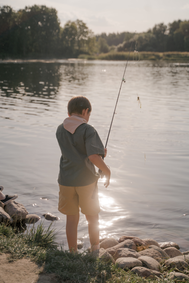 Ein kleiner Junge beim Fischen am Ufer eines Gewässers mit Angelrute und Köder.