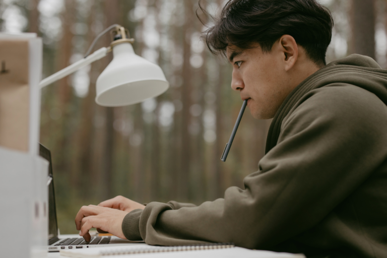 Ein junger Mann, der auf einem Laptop arbeitet und tippt, während er sitzt.