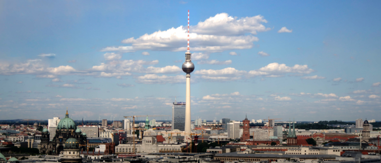 Eine Fernaufnahme vom Fernsehturm in Berlin, um den herum weitere Gebäude stehen.