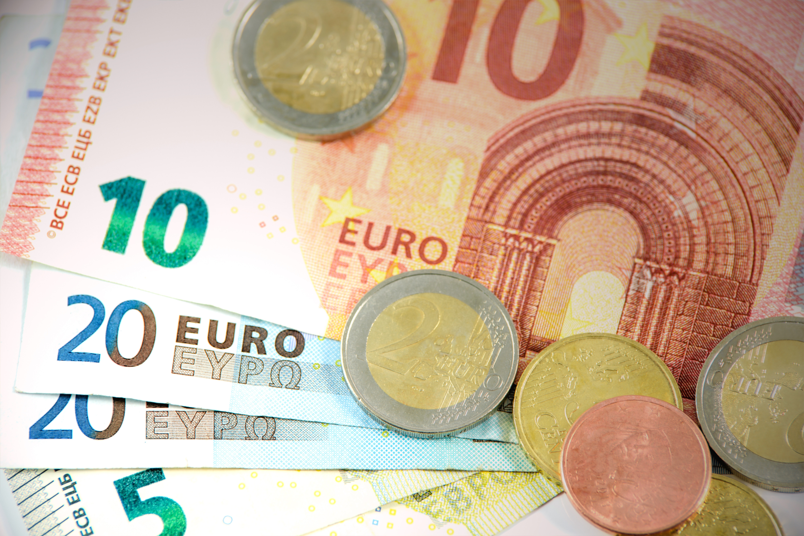 Mehrere Euro-Banknoten und -Münzen auf einem hellen Hintergrund.
