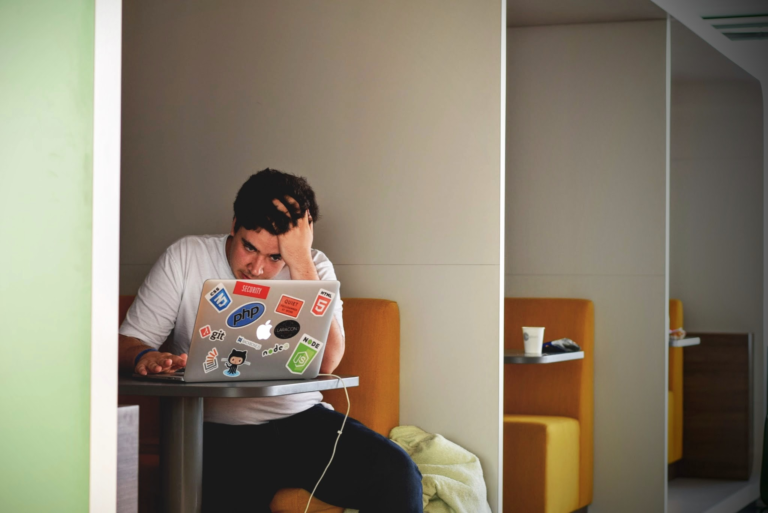 Ein Mann sitzt an einem Schreibtisch und arbeitet auf einem MacBook Pro. Das weiße Hemd des Mannes ist sichtbar, während er sich konzentriert.