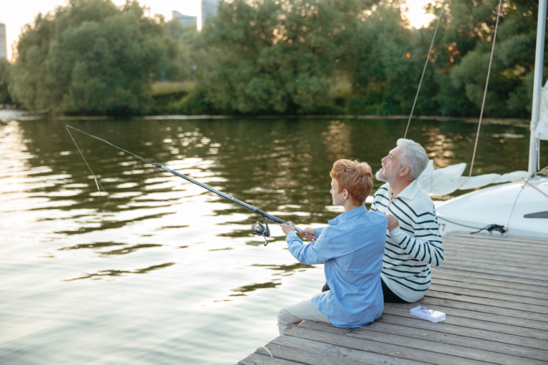 Ein Mann und ein Kind sitzen am Seeufer und angeln, während sie auf das ruhige Wasser schauen.