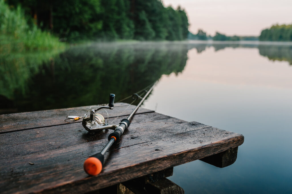 Fishing rod, spinning reel on the background pier river bank. Sunrise. Fog against the backdrop of lake. Misty morning. wild nature. The concept of rural getaway. Article about fishing day.