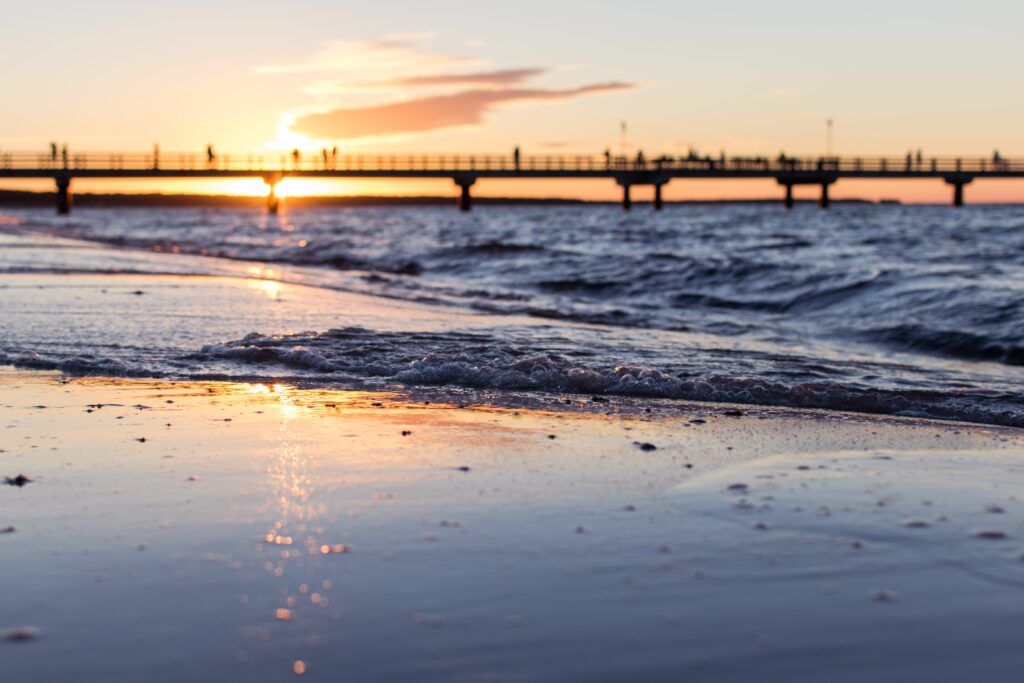 Ein Strand an der Ostsee mit einem Steg im Hintergrund bei Sonnenuntergang.